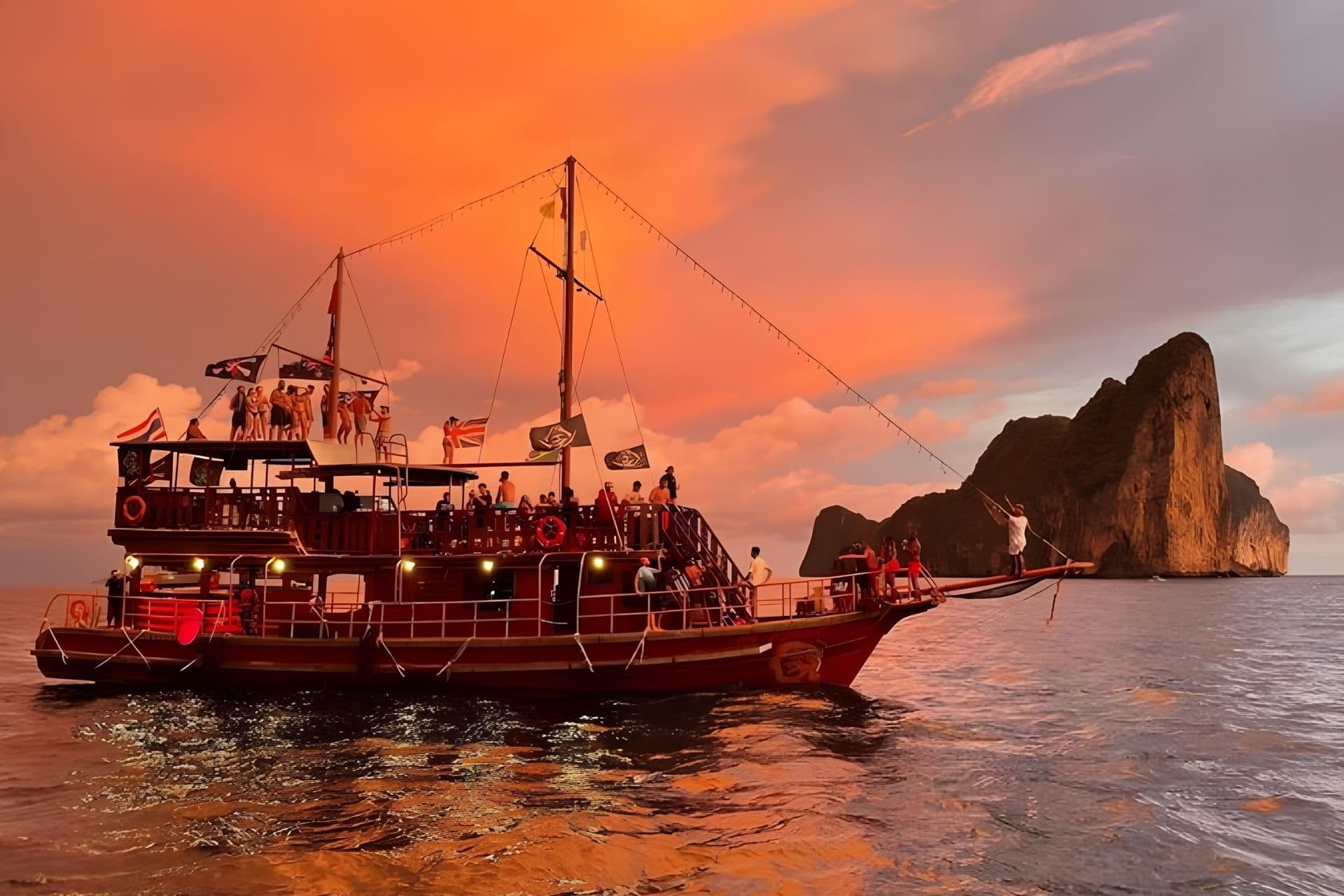 The Phi Phi Pirates ship at golden-hour sunset beside Bida Rock, guests on deck