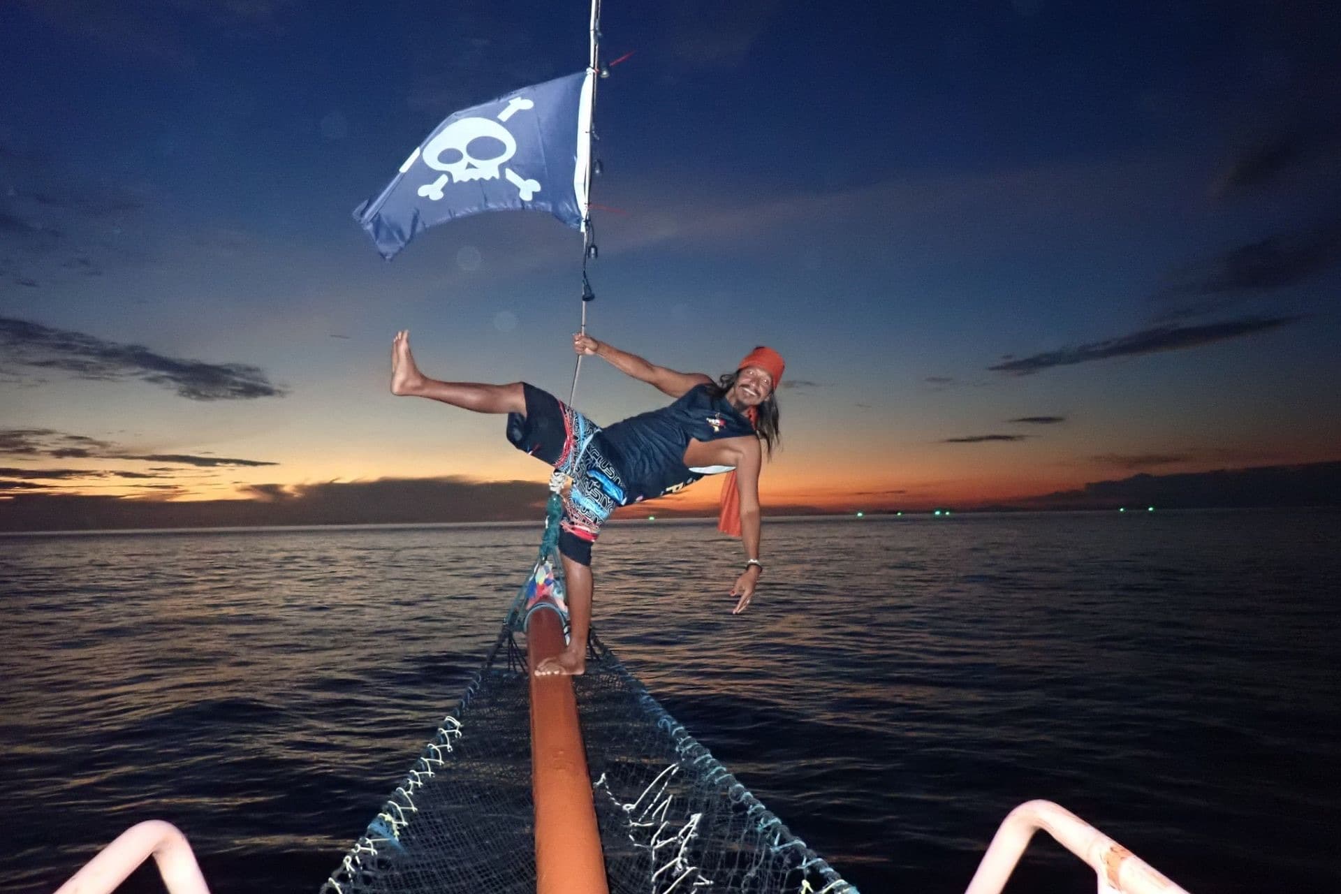 A guest balancing on the bowsprit net under the skull flag